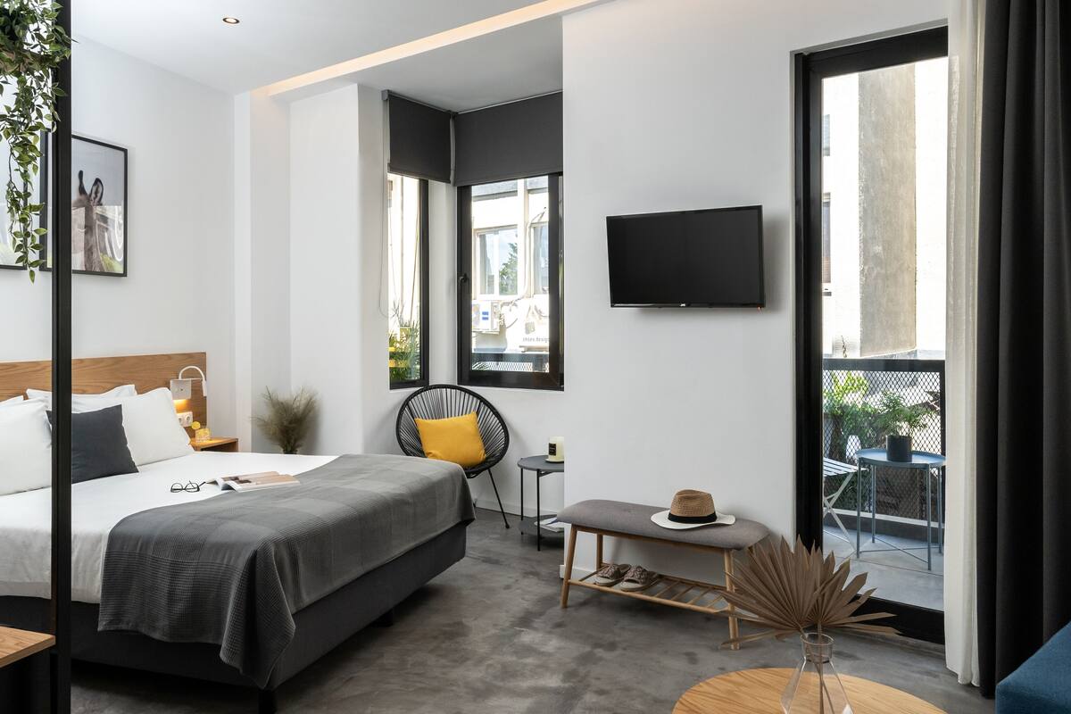 Una habitación de hotel moderna con una cama grande, una mesita con un sombrero, una silla y un televisor en la pared.