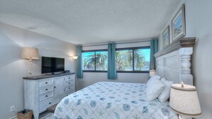 Une chambre à coucher avec un lit, une télévision, une commode et une fenêtre avec des rideaux.