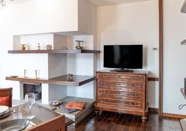Un salon avec une cheminée, un téléviseur posé sur un meuble en bois, et un coin repas avec une table et des chaises.