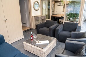 A modern living room with a dark grey sofa set, a wicker coffee table, and a small dining table. - Diane's Cottage (Knokke-Heist)