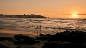 Escena de playa con olas, un atardecer y una costa distante.