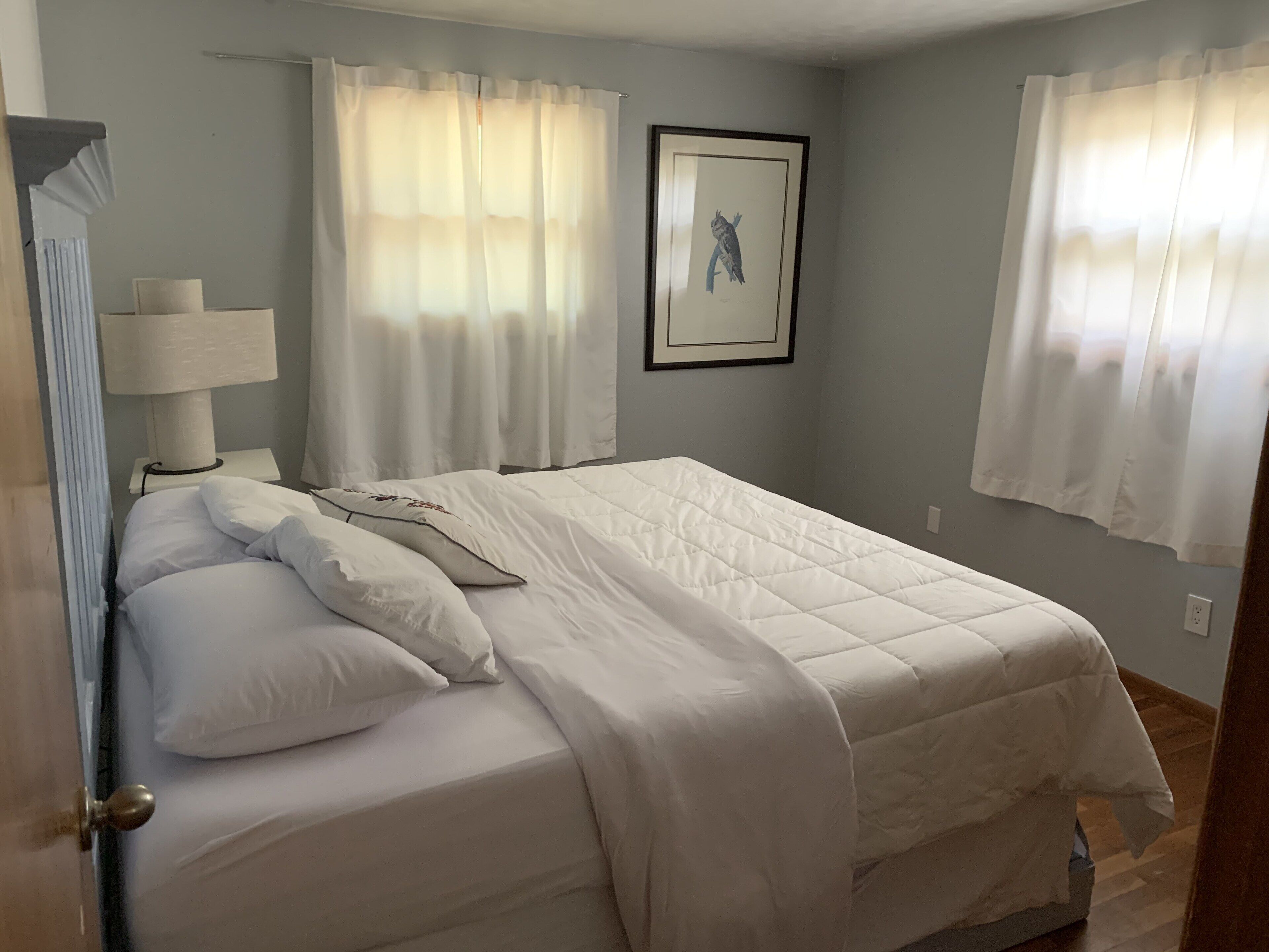 A neatly made bed with white bedding, a bedside lamp, and a framed picture on the wall.