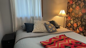 A neatly made bed with a quilted bedspread and pillows, a bedside lamp, and a floral-patterned wall. - Comfortable and Quaint w/ a Hot Tub (Brookings)