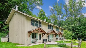 A two-story building with a sloped roof, large windows, and a covered porch area. - 2 bedroom Killington condo with fireplace, kitchen, and Wi-Fi. (Killington)
