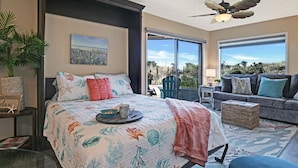 A bedroom with a bed, a nightstand, a potted plant, and a view of the outdoors. - Remote Oceanfront Retreat Between Santa Cruz & Monterey (Watsonville)