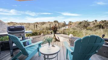 A deck with two turquoise Adirondack chairs, a small round table, and a grill.