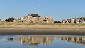 A beachfront property with multiple buildings, a sandy beach, and a calm body of water reflecting the structures. - Remote Oceanfront Retreat Between Santa Cruz & Monterey (Watsonville)