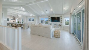 A spacious living area with a large sofa, a television, and a dining area with a table and chairs. - Nearly Beachfront, One house from the beach! Pool and Game Room - Ocean Overlook (Siesta Key)