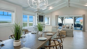 A spacious dining area with a wooden table set for four, surrounded by comfortable seating. Large windows offer a view of the ocean. - Nearly Beachfront, One house from the beach! Pool and Game Room - Ocean Overlook (Siesta Key)