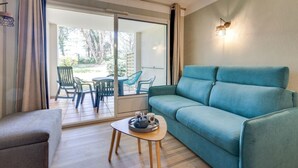 Un soggiorno moderno con un divano color petrolio, un tavolino in legno e una porta scorrevole in vetro che dà su un’area salotto esterna.