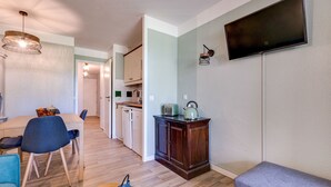 Un soggiorno moderno con zona pranzo, pavimento in legno, TV a schermo piatto montata a parete e cucina sullo sfondo.