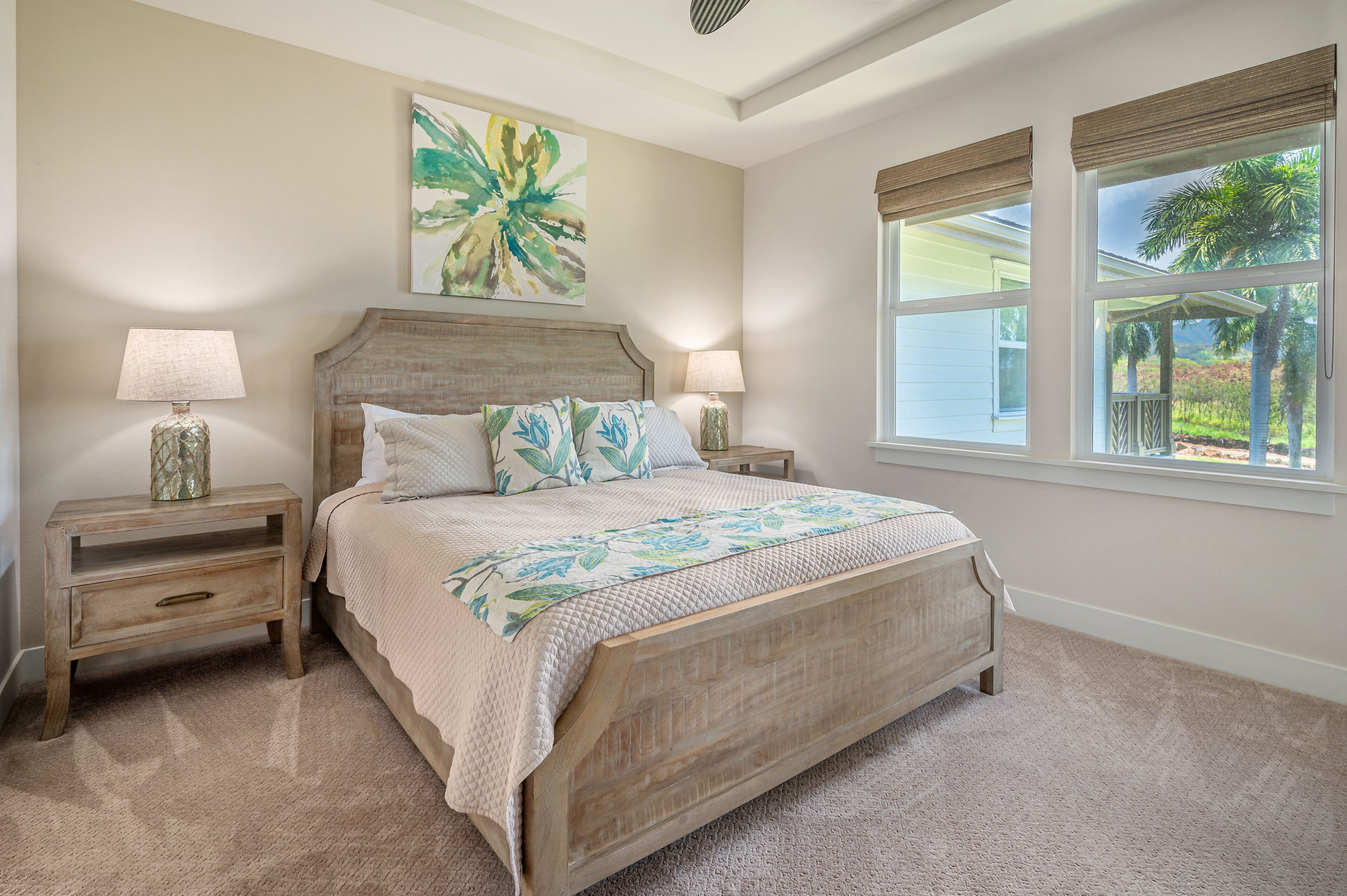 A bedroom with a wooden bed, two bedside tables, a large window with a view of palm trees, and a floral painting on the wall.