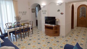 Ein Wohnzimmer mit Essbereich, einem Fernseher auf einem Holzgestell und einem gemusterten Boden.