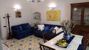 Ein Wohnzimmer mit blauem Sofa, einem Esstisch mit Stühlen, einer Chandelüster und Wanddekoration.