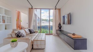 Un salon moderne avec un canapé, un pouf et un téléviseur fixé au mur.