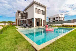 A modern two-story house with a swimming pool, outdoor seating, and a pink flamingo float. - SA03 - Excelente Casa 4 Suítes - Sauípe (Mata de São João)