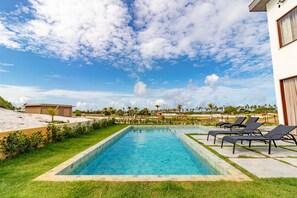 A rectangular swimming pool with a tiled edge, surrounded by a grassy area and a few lounge chairs. - SA03 - Excelente Casa 4 Suítes - Sauípe (Mata de São João)