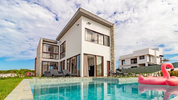 Une maison moderne à deux étages dotée d’une piscine, d’un espace de détente extérieur et d’un flotteur en forme de flamant rose.