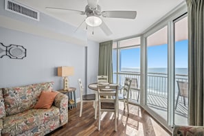 Enjoy ocean views from the large window in this inviting room, featuring a sofa, dining table, and ceiling fan.