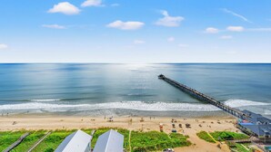 Una playa con un muelle que se adentra en el océano, arena dorada y algunos edificios al frente.