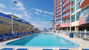 Una piscina con sillas reclinables azules y un edificio con balcones al fondo.