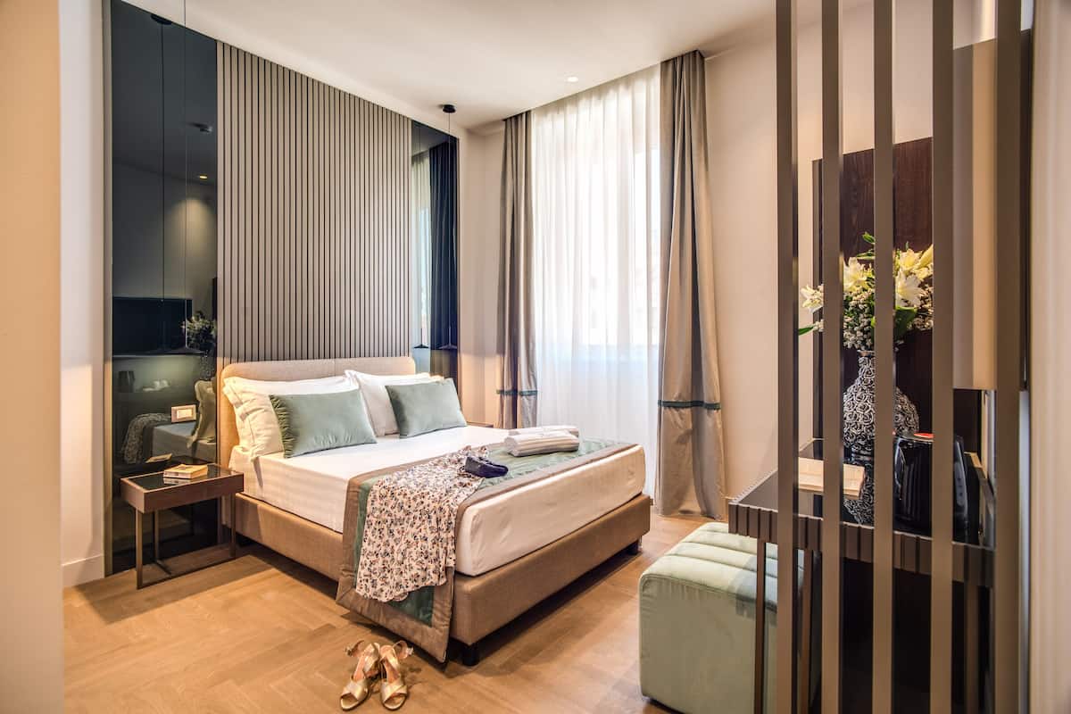 Moderni hotellihuone, jossa on suuri sänky, yöpöytä, pieni työpöytä ja oleskelualue, jossa on tuoli.