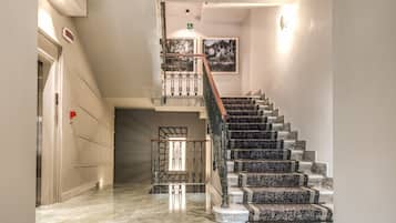 Un interno moderno con una scala in marmo, una ringhiera in vetro e un quadro appeso al muro.