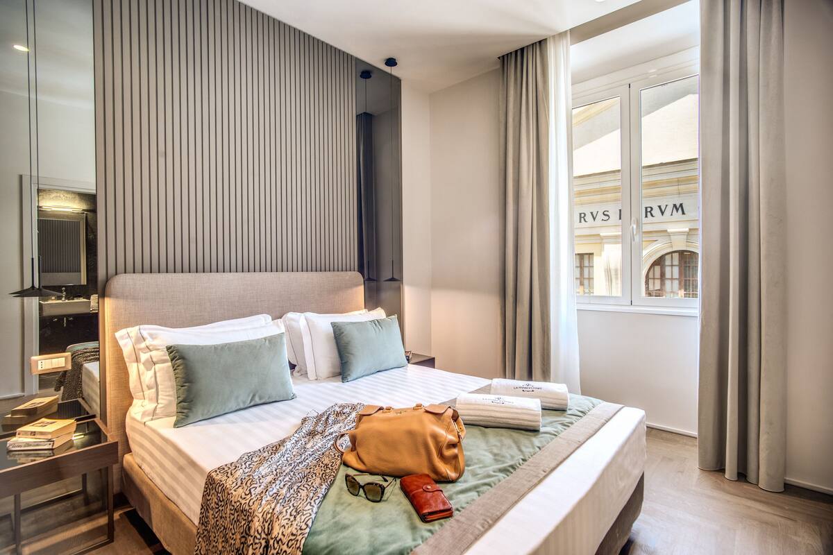 Moderni hotellihuone, jossa on suuri sänky, yöpöytä, peili ja ikkuna, jossa on verhot.