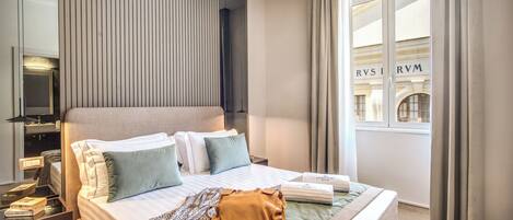 Una habitación de hotel moderna con una cama grande, una mesita de noche, un espejo y una ventana con cortinas.
