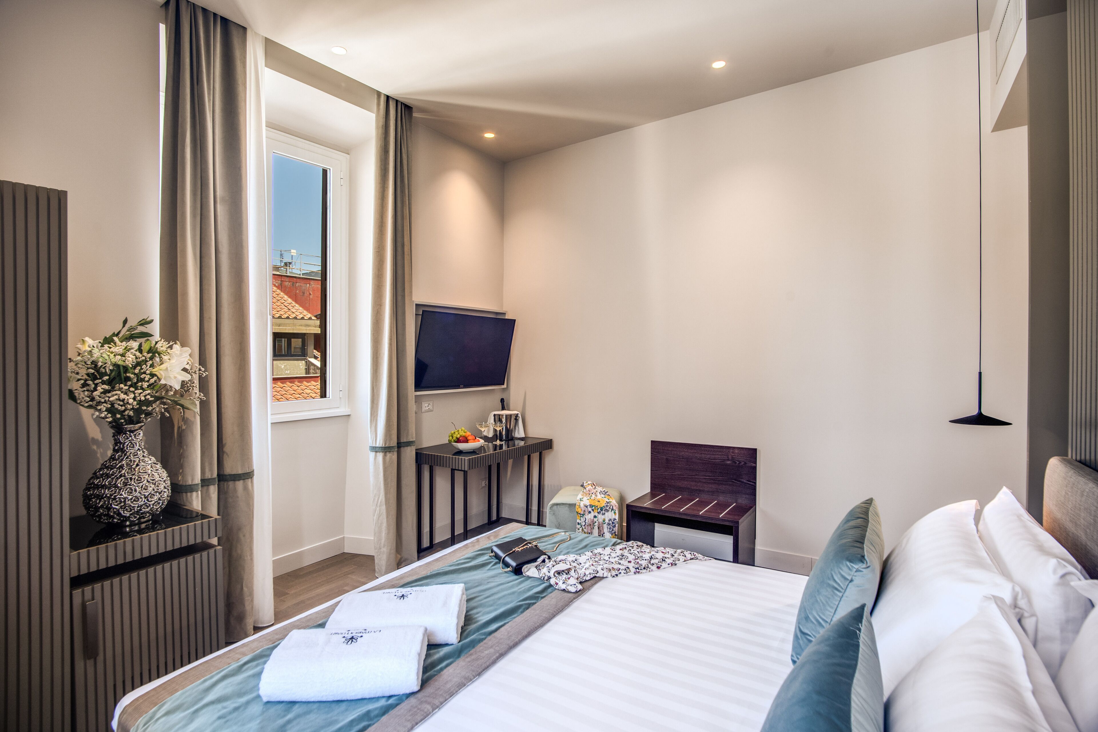 A modern hotel room with a large bed, a flat-screen TV, a desk with a chair, and a window with curtains.