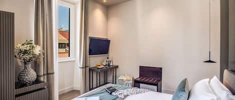 A modern hotel room with a large bed, a flat-screen TV, a desk with a chair, and a window with curtains.