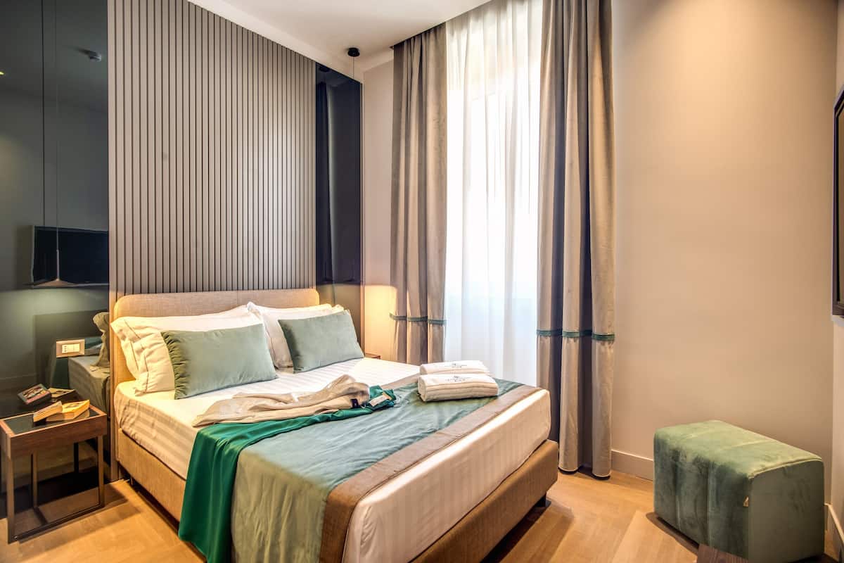Moderni hotellihuone, jossa on suuri sänky, yöpöytä, vihreä rahi ja seinälle asennettu televisio.