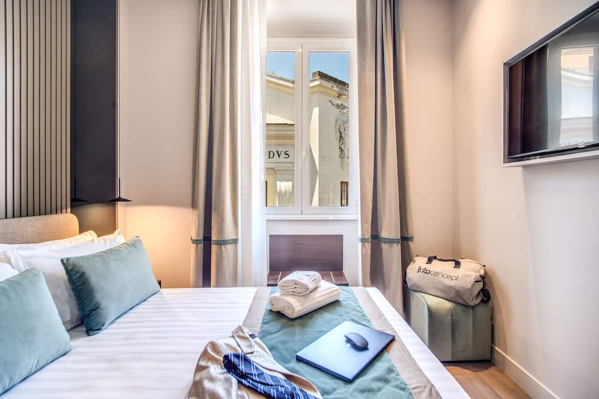 Hotellihuone, jossa on sänky, työpöytä kannettavalla tietokoneella, matkalaukku ja seinälle asennettu televisio.