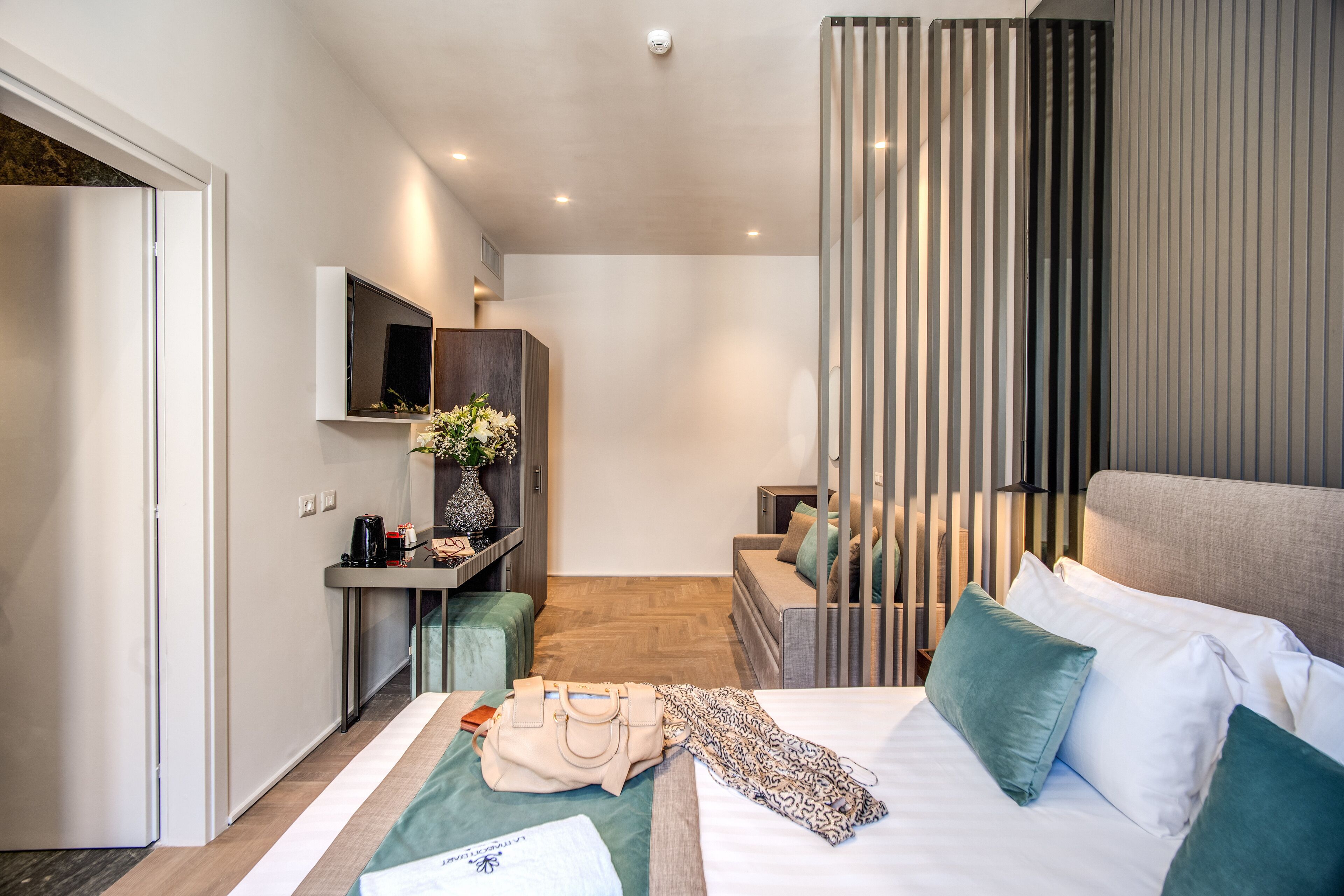 A modern hotel room with a bed, a desk, a TV, and a view of the city.