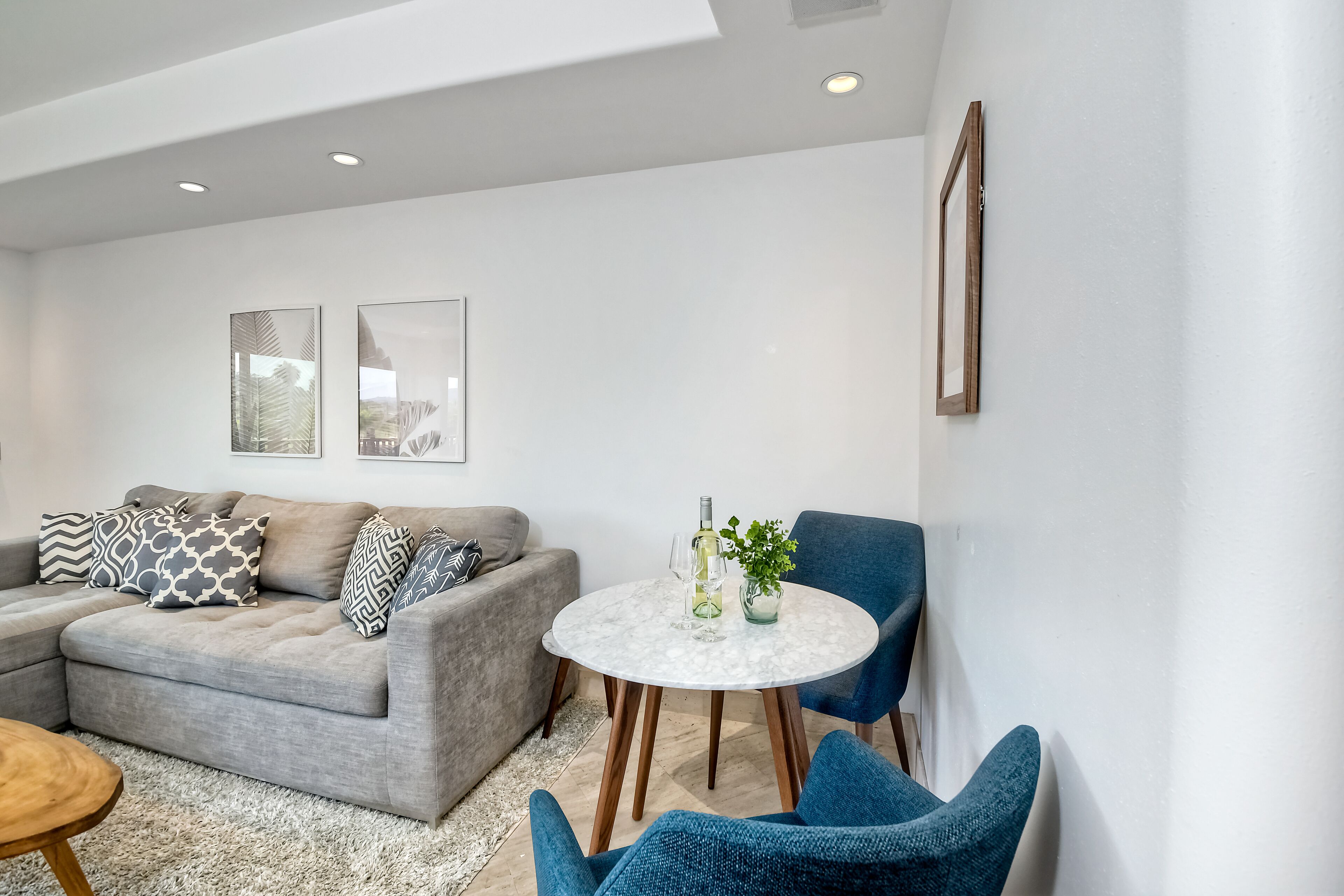 A modern living room with a grey sectional sofa, a round marble coffee table, and blue armchairs.