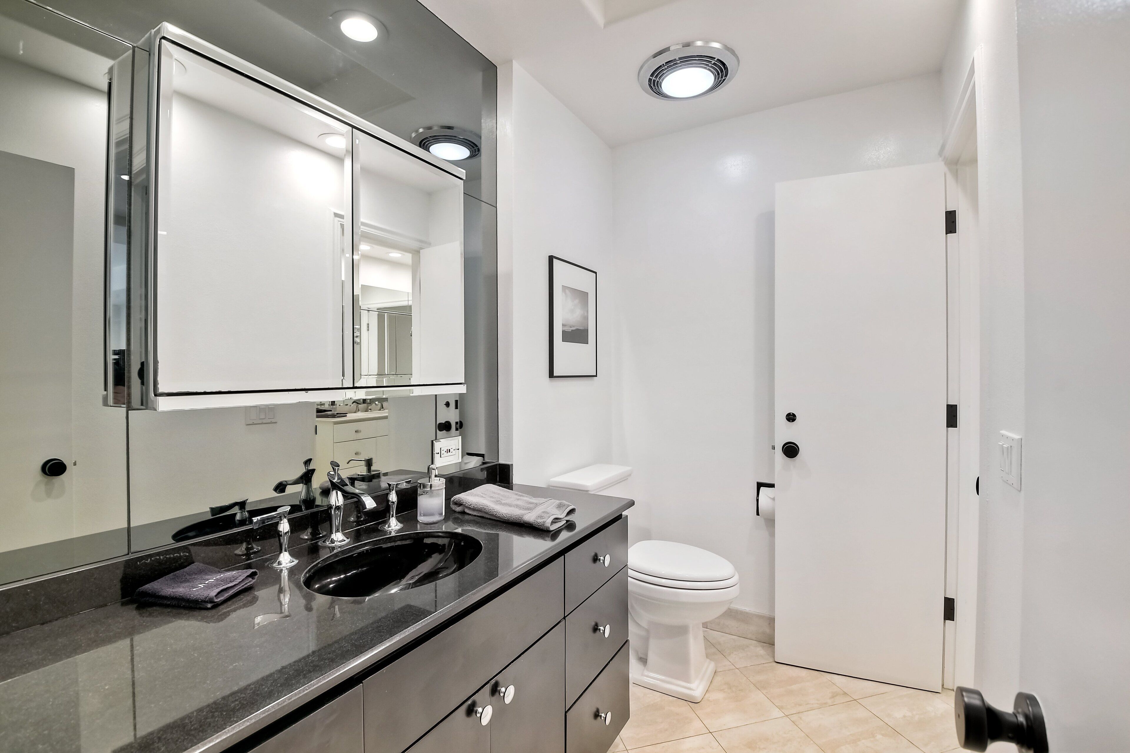 Un baño moderno con tocador doble, inodoro y puerta con manija.