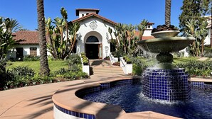 A spa with a fountain, a white building with a red-tiled roof, and a well-maintained garden. - Private Balcony Overlooking Pool | Gated Parking (Carlsbad)