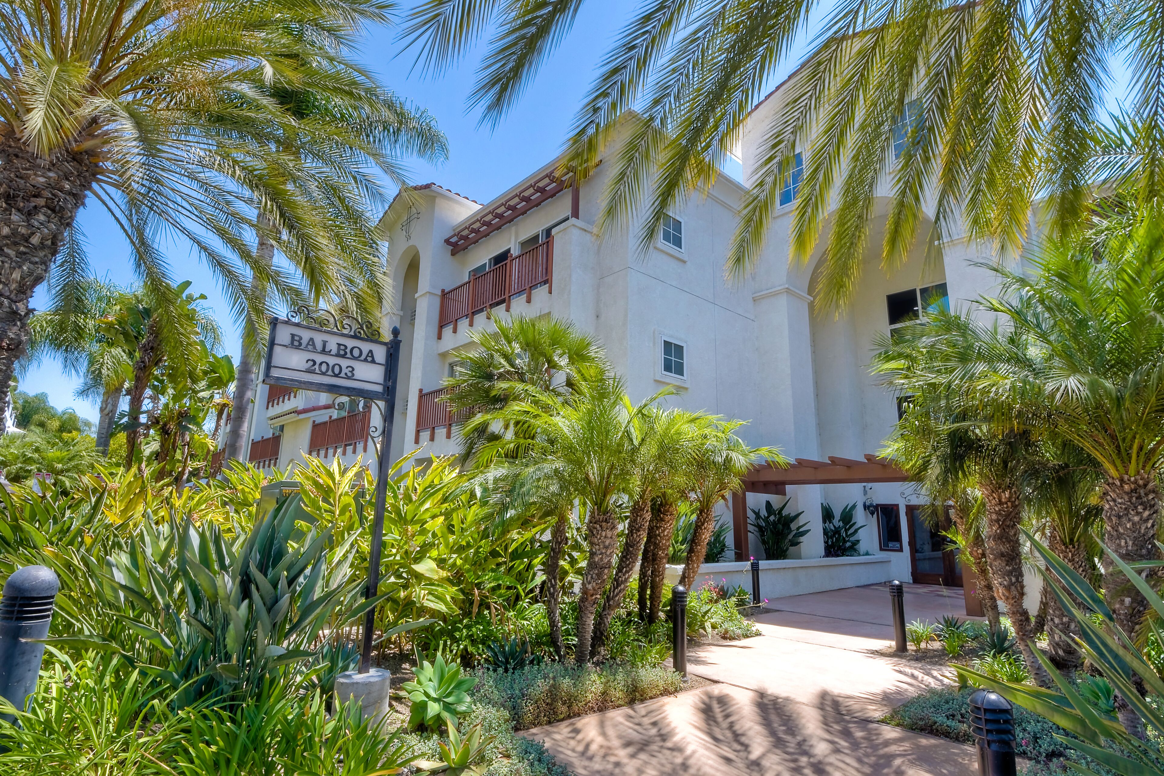 A hotel with a sign reading "BALBOA 2003," surrounded by lush greenery and palm trees.