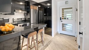 A modern kitchen with a large island, stainless steel appliances, and a white door with a window. - Private Balcony Overlooking Pool | Gated Parking (Carlsbad)