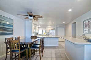 A modern kitchen with a central island, wooden dining table with chairs, and a ceiling fan. - Oceanfront Views, Heated Pool, Hot Tubs, BBQ (Solana Beach)
