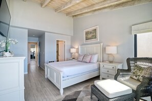 A bedroom with a large bed, bedside tables, a wicker chair, and a painting on the wall. - Oceanfront Views, Heated Pool, Hot Tubs, BBQ (Solana Beach)