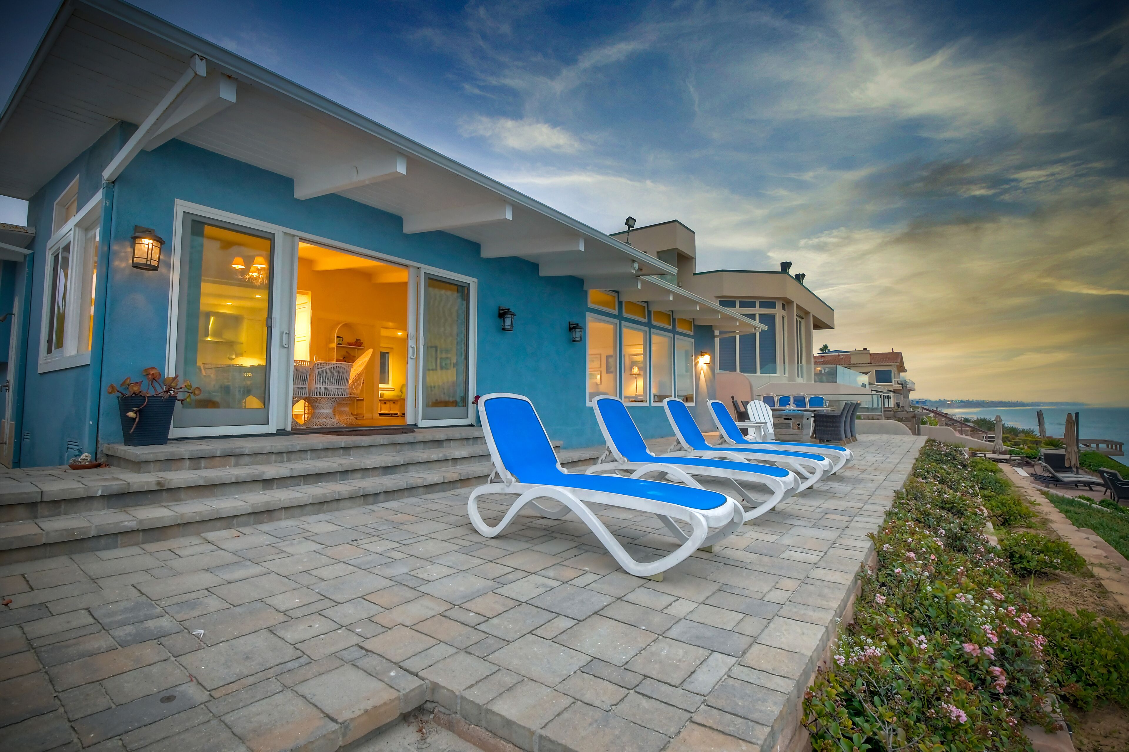 Un hôtel en bord de mer, avec une façade bleue, un espace extérieur couvert doté de fauteuils et offrant une vue sur l’océan.