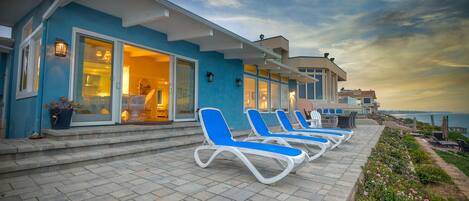 Un hôtel en bord de mer, avec une façade bleue, un espace extérieur couvert doté de fauteuils et offrant une vue sur l’océan.