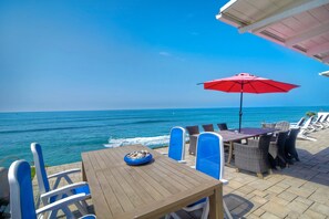 Une table en bois, des chaises bleues et un parasol rouge, le tout offrant une vue sur l’océan.