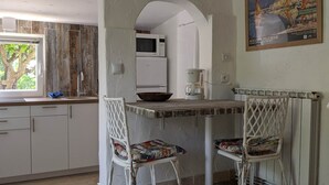 Eine Küche mit weißen Schränken, einem weißen Esstisch, zwei Stühlen, einer Kaffeemaschine und einem Bild an der Wand.