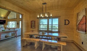 L’intérieur d’un chalet en bois, avec une grande table à manger, des bancs et un lustre.