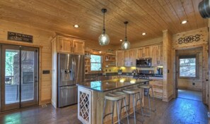 Une cuisine spacieuse dotée de meubles en bois, d’un îlot central avec des tabourets, d’appareils électroménagers en acier inoxydable et de luminaires suspendus.