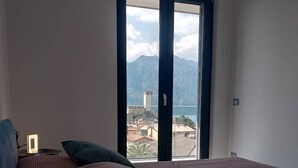A bedroom with a large window, a bed with a pink bedspread, and a nightstand with a lamp. - BLUE SKY SAPPHIRE APP.  LAKE VIEW CIR:023045-LOC-00628 CIN: EN023045C2HTNJMTGL (Malcesine)