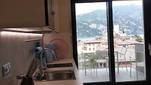 A modern kitchen with a stainless steel sink and a view of a coastal town through a large sliding glass door. - BLUE SKY SAPPHIRE APP.  LAKE VIEW CIR:023045-LOC-00628 CIN: EN023045C2HTNJMTGL (Malcesine)