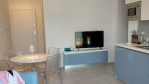 A modern living room with a sofa, a glass dining table, and a TV. - BLUE SKY SAPPHIRE APP.  LAKE VIEW CIR:023045-LOC-00628 CIN: EN023045C2HTNJMTGL (Malcesine)